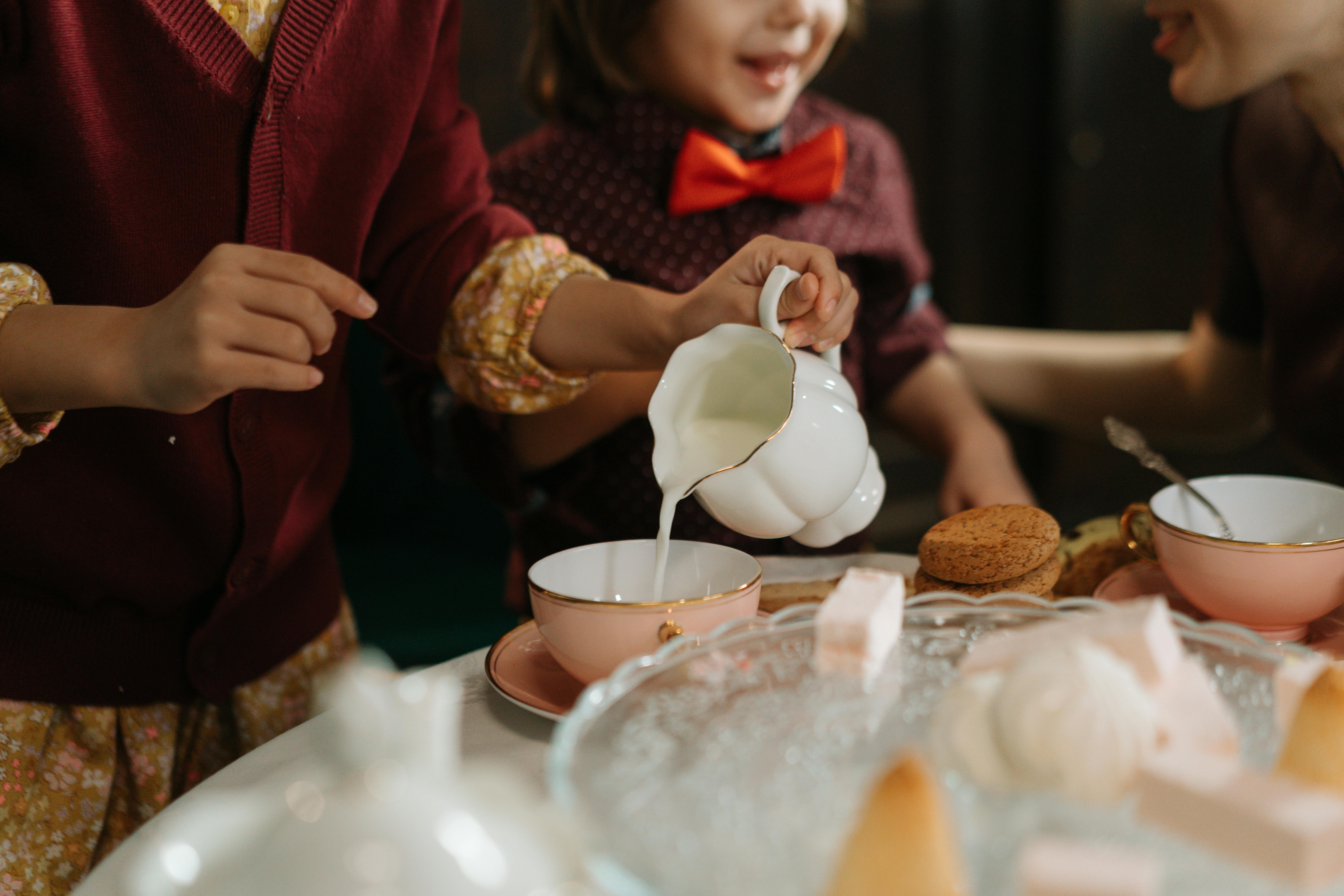 A cheerful tea party with children pouring milk into cups, surrounded by cookies and desserts.