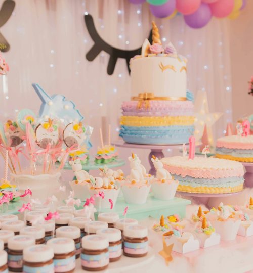 A vibrant unicorn-themed birthday party setup with cakes, cupcakes, and decorations.