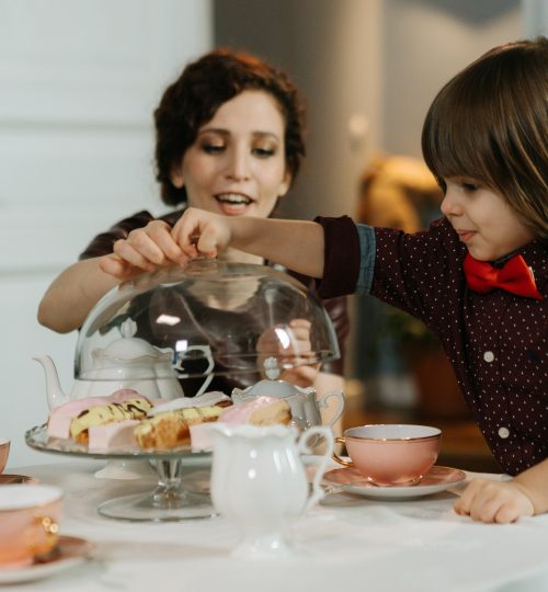 A mother and child sharing tea and pastries at an indoor table, enhancing family moments.