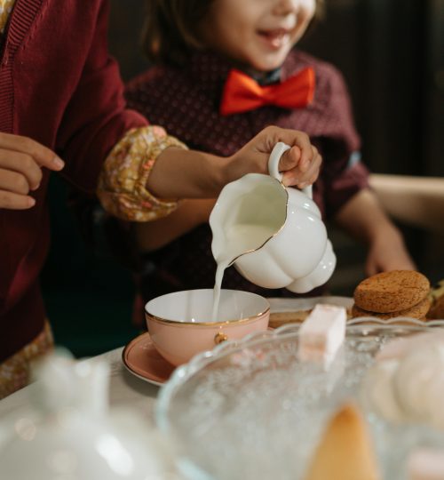 A cheerful tea party with children pouring milk into cups, surrounded by cookies and desserts.