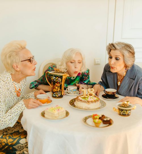 Three senior women celebrate a birthday indoors with cake and tea. A joyful celebration of life and friendship.